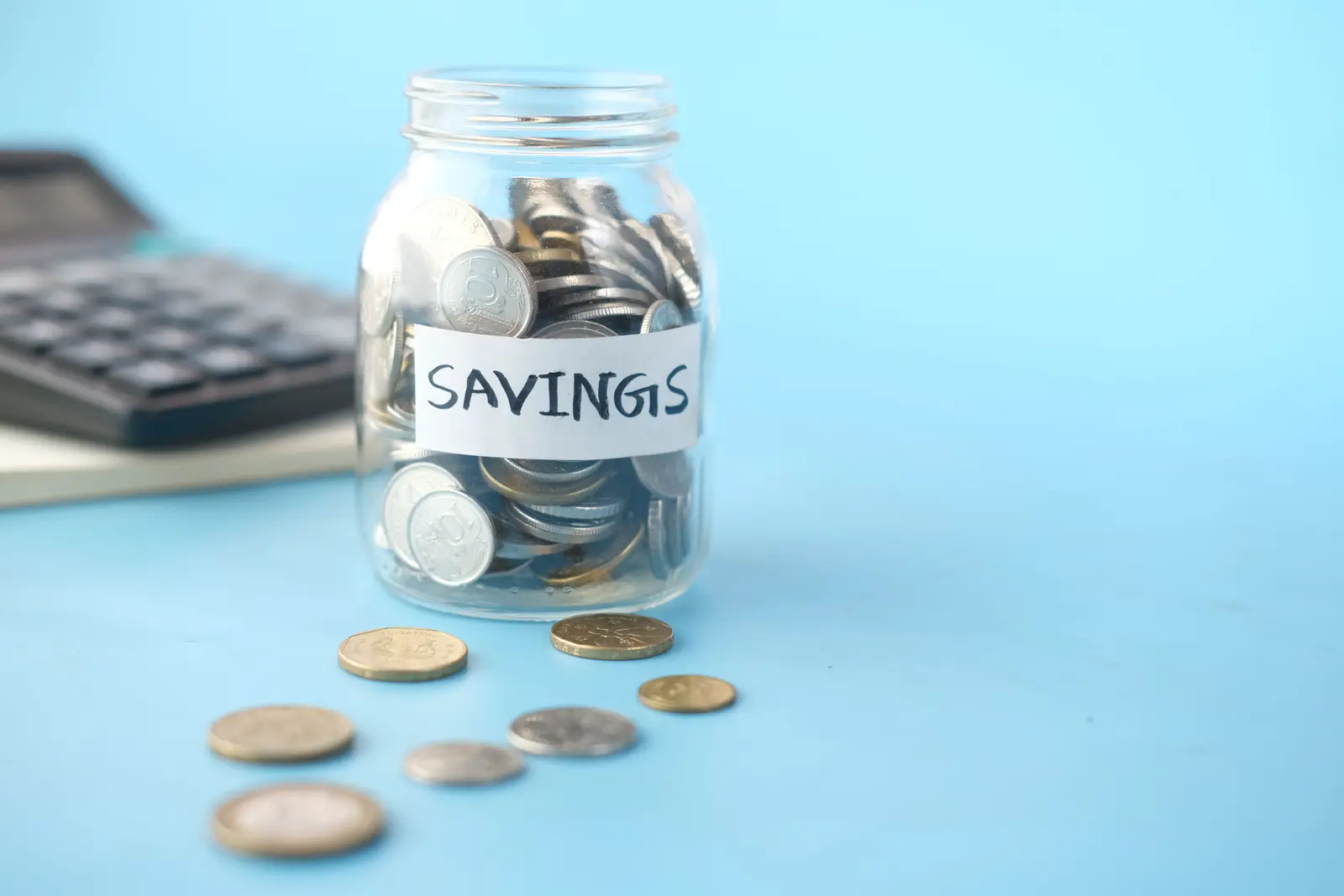 A glass jar of coins labelled savings beside a calculator