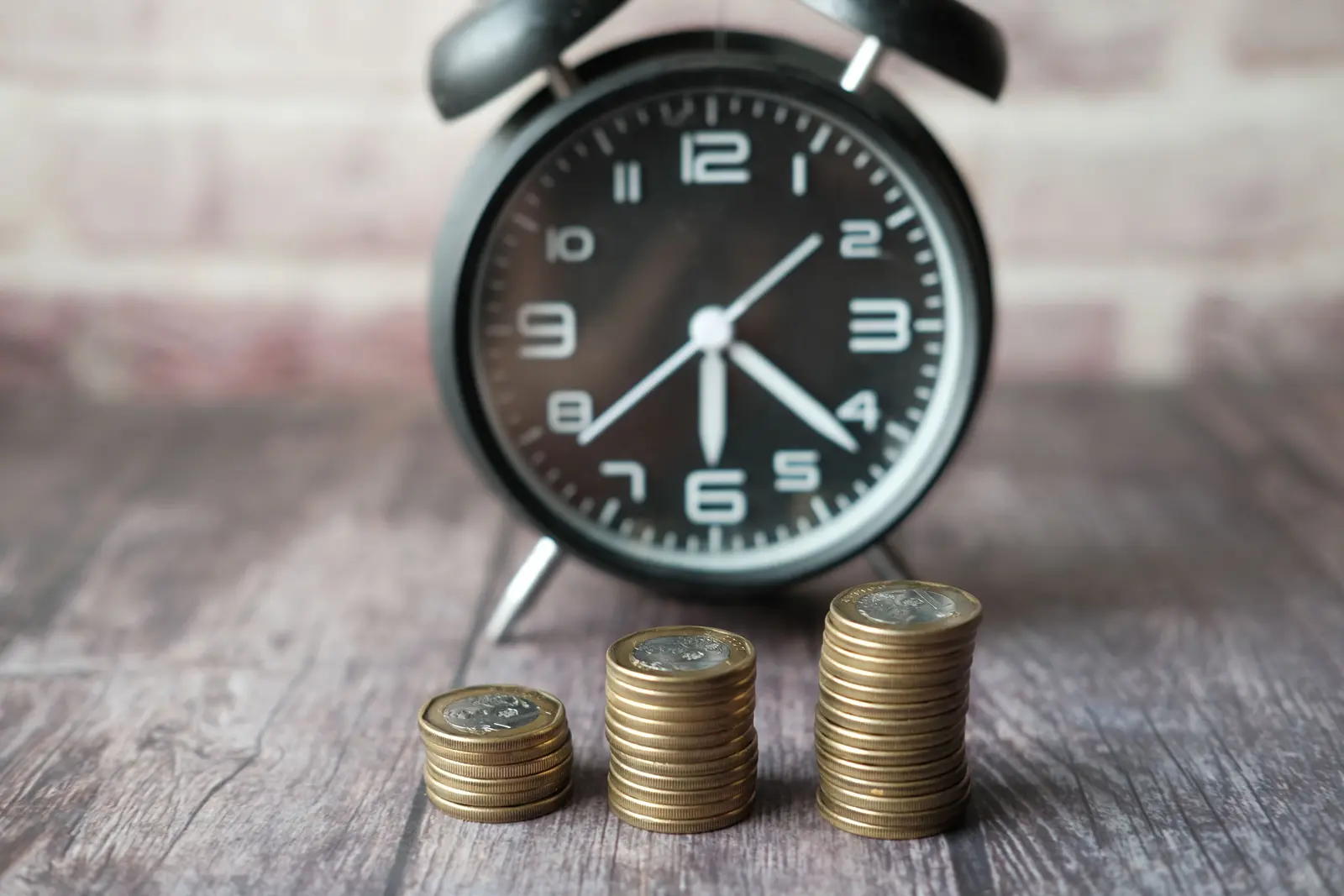 An alarm clock beside three stacks of coins