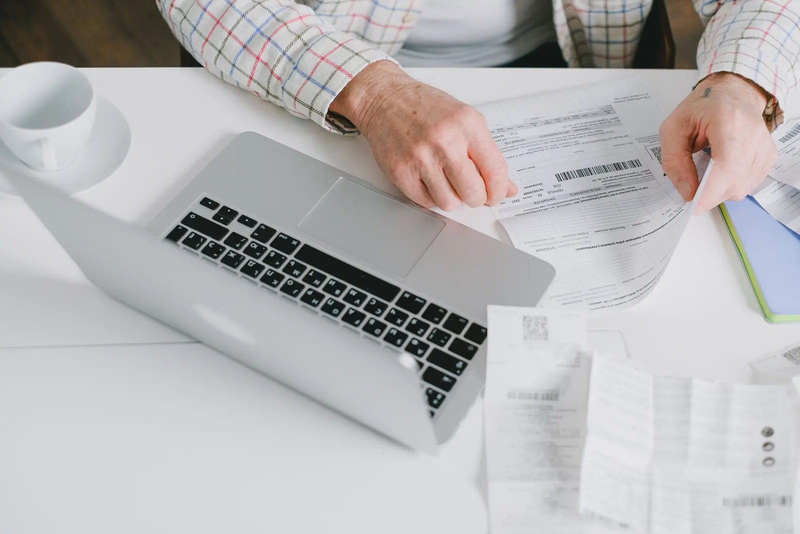 Hands sorting printed documents beside a laptop