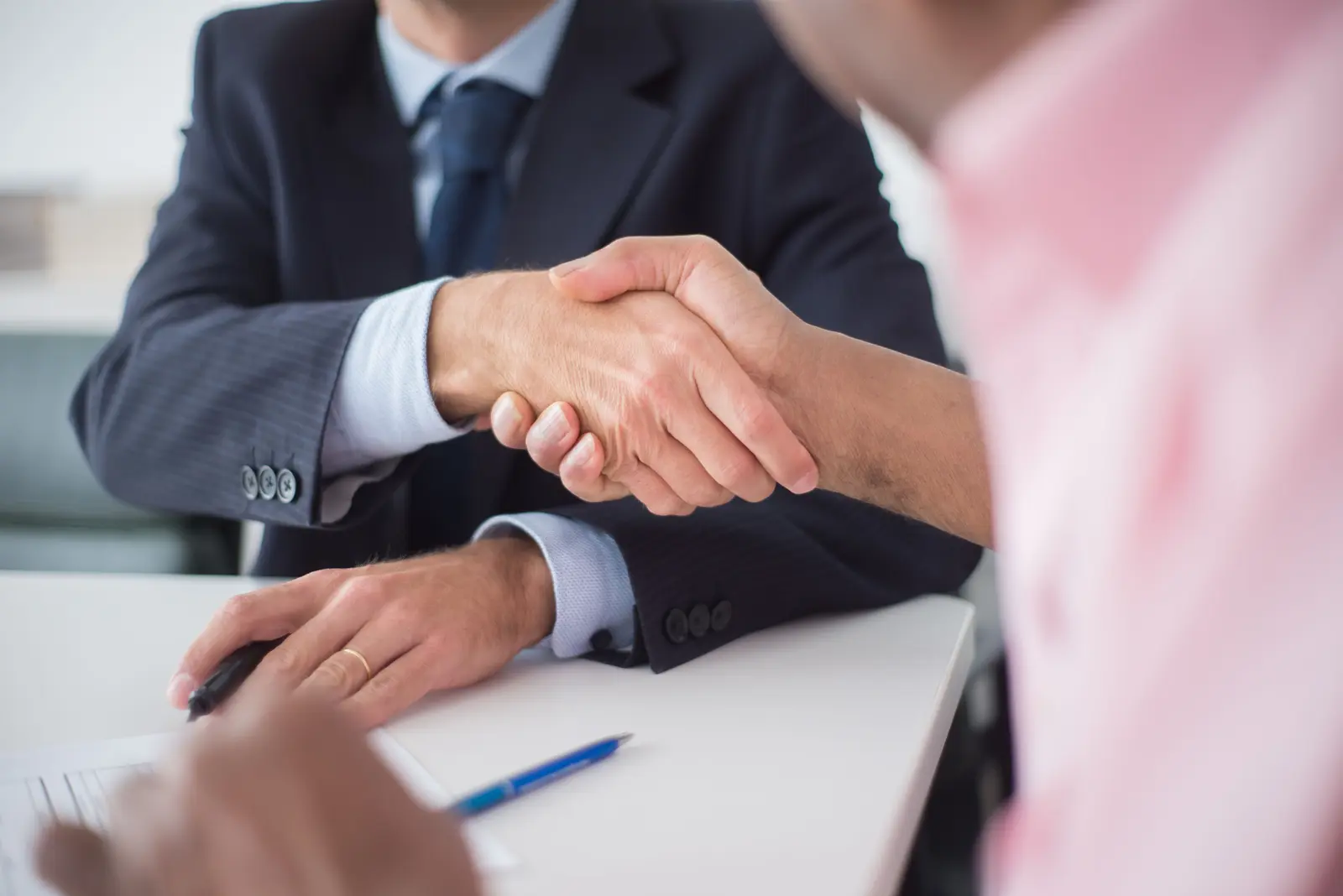 Two people shaking hands across a desk after a meeting